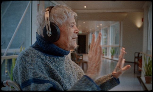 Protagonist hat Kophörer, sitzt und tanzt mit Händen auf dem Seniorenheimflur