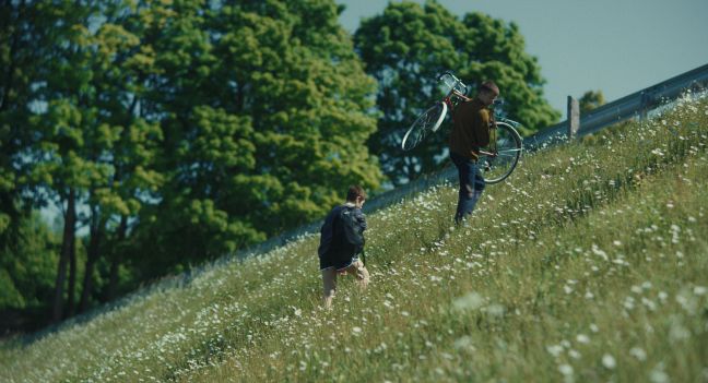 Ada und Marius gehen einen Hügel hoch, Marius trägt sein Fahrrad