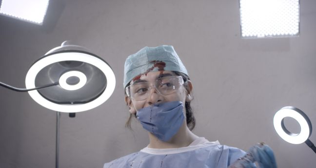 Karla lächelt hinter einer OP-Maske, ihr Gesicht ist blutverschmiert