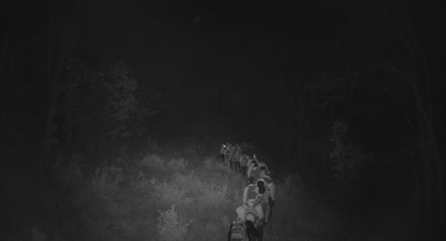 Durch eine Nachtsichtkamera: Eine Gruppe Männer geht in einer Schlange mit Rucksäcken