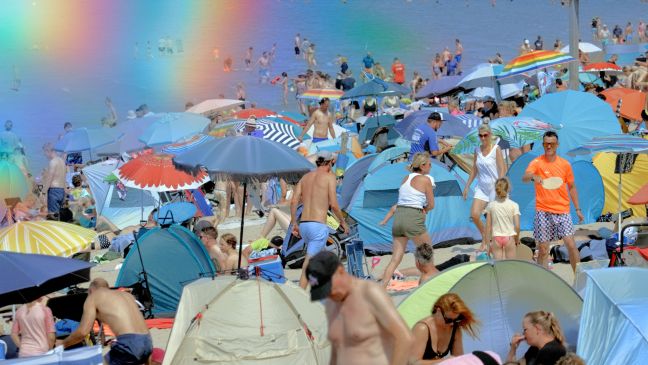 Ein überfüllter Strand, links im Bild sind Regenbogen-Linsenreflektionen