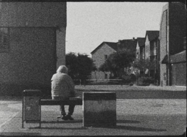 schwarz-weiß, eine ältere Person auf einer Bank auf einem Marktplatz