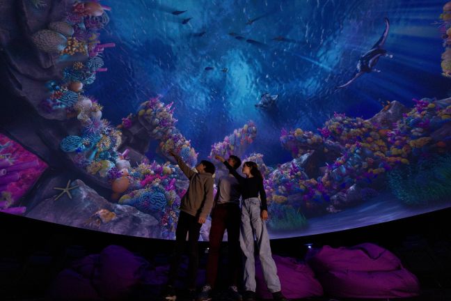 Zwei Kinder und ein Erwachsener im Planetarium, sie zeigen auf die Leinwand mit einem Korallenriff