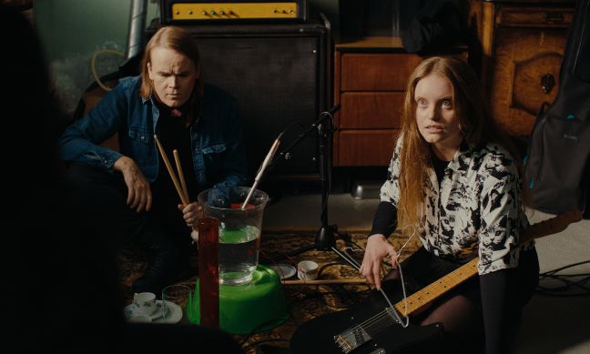 Sini guckt auf dem Boden mit Schlagzeugsticks in der Hand; Iiris mit Gitarre auf der Schoß