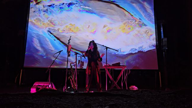 Veera Neva singt vor Leinwand mit fließenden Formen