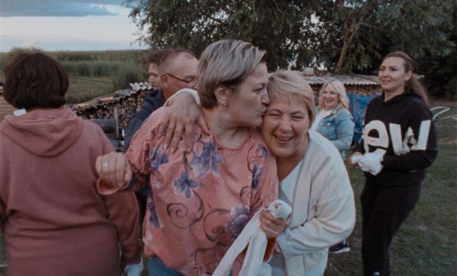 Eine Gruppe von Menschen freut sich, im Fokus umarmen sich zwei Frauen, die linke küsst die andere auf die Stirn