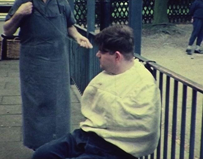 Ein junger Mann wird mit Jacke und Riemen draußen an einem Gitter fixiert