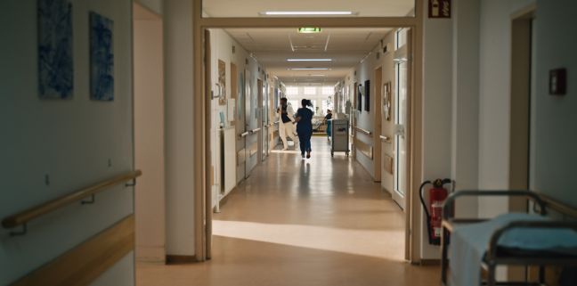 In einem Krankenhausflur laufen ein Arzt und eine Krankenschwester in Richtung eines Zimmers