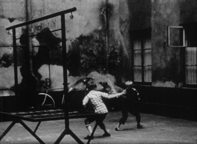 Zwei Kinder spielen mit Stöcken in einem Hof