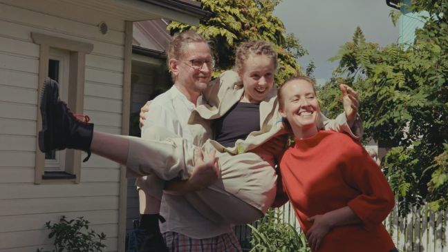 Roosi mit 16 feiert auf dem Arm ihres Vaters ihren ersten Schulabschluss, posiert mit Eltern