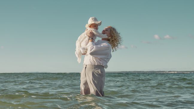 Vibeke steht im Wasser und hält Elliot nach oben