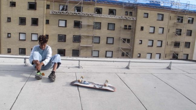 Phillip ist auf einem Gebäudedach mit seinem Skateboard, im Hintergrund ein Hochhaus
