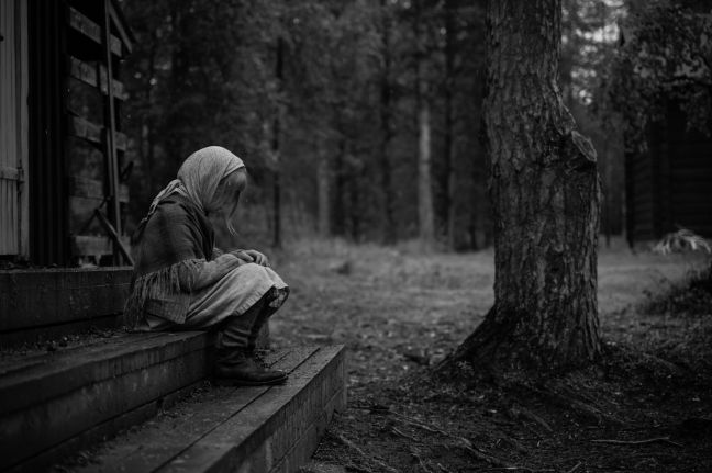 Kind sitzt auf den Treppen des Hauses; im Hintergrund ein Baum