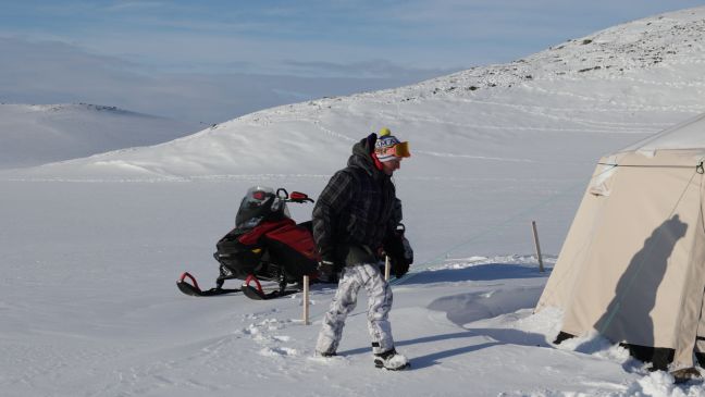 ein Mann mit einem Schneescooter vor einem Zelt in einer Schneelandschaft